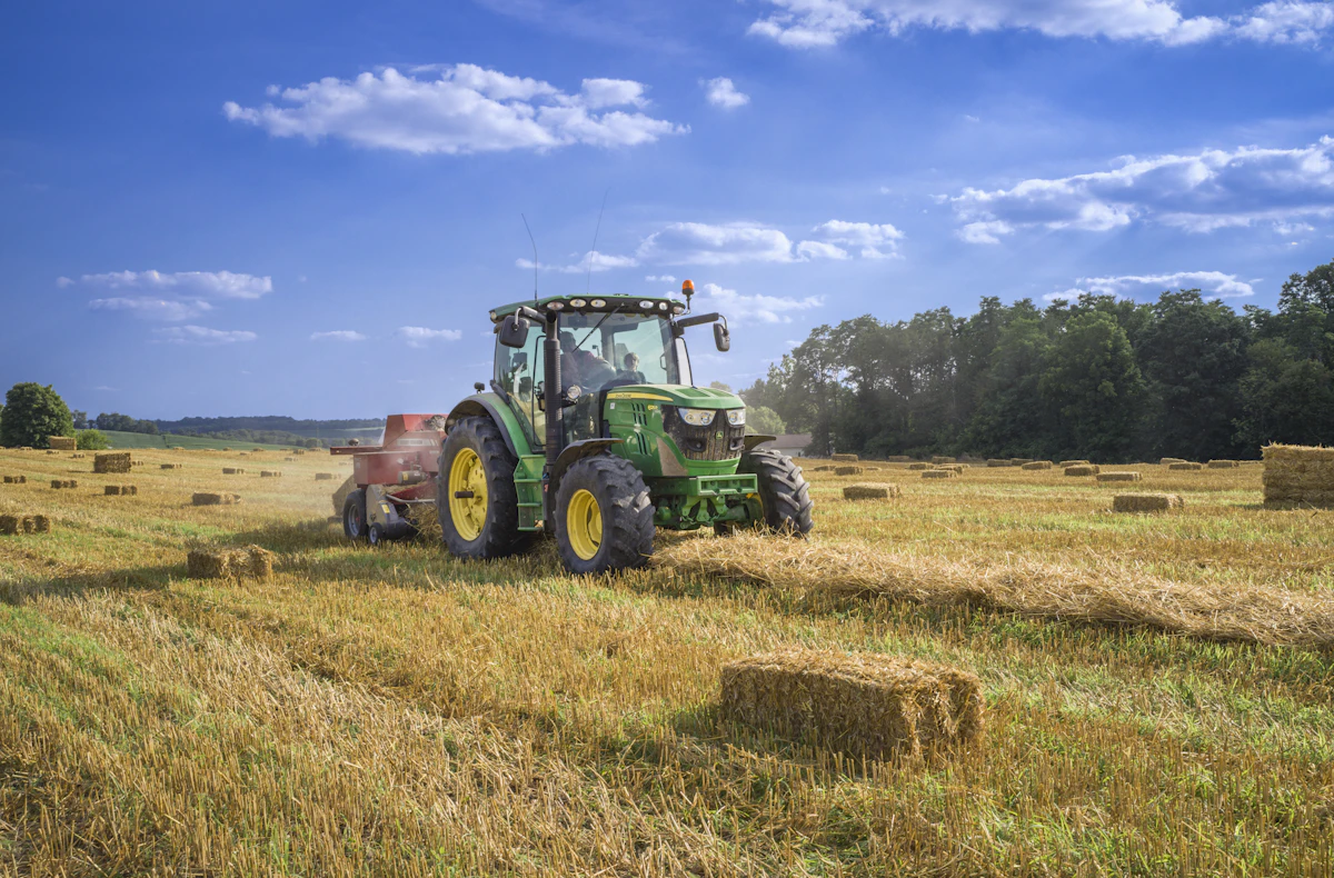 Grüner Traktor auf einem abgeernteten Feld mit Heuballen